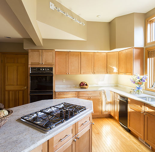 Bright, modern kitchen featuring wooden cabinets, granite countertops, a gas stove, and natural light from large windows.